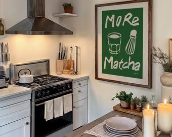 May include: A green and white poster with the text "More Matcha" and a drawing of a glass of matcha and a whisk. The poster is hanging on a white wall in a kitchen.