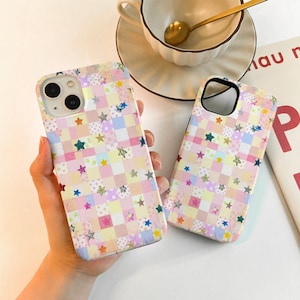 Könnte beinhalten: Zwei Handyhüllen mit einem Patchwork-Design mit Quadraten in Pastellfarben wie Rosa, Gelb und Blau. Die Hüllen sind mit Sternformen in verschiedenen Farben verziert. Die Handyhüllen werden von einer Person gehalten.