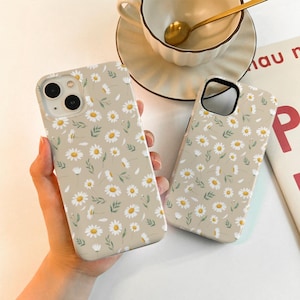 May include: Two beige phone cases with a white daisy pattern. The cases are made of a soft, flexible material and have a matte finish.