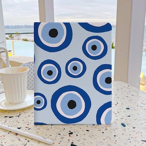 May include: A blue and white notebook with a pattern of evil eyes. The notebook is on a light brown speckled surface.