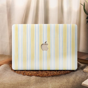 May include: A laptop case with a vertical striped pattern in yellow, white, and light blue. The case has a cutout for the Apple logo. The case is on a brown woven mat.
