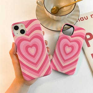 May include: Two pink and white phone cases with a heart design. The cases have a concentric circle pattern with a heart shape in the center.
