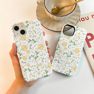 Peut inclure: Deux coques de téléphone blanches avec un motif floral jaune. Les coques ont une découpe pour l'objectif de l'appareil photo.