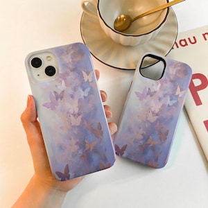 May include: Two phone cases with a purple and pink watercolor butterfly design. The cases are made of a hard plastic material and have a matte finish.
