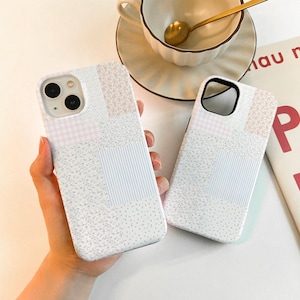 May include: Two white phone cases with a patchwork design featuring pink and blue floral patterns, gingham, and stripes.