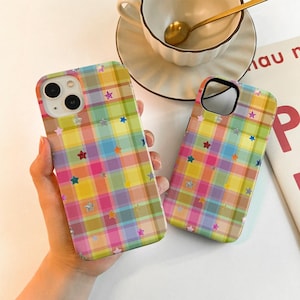May include: Two phone cases with a colourful plaid pattern in yellow, pink, blue, and green. The cases are decorated with small star shapes in various colours. One case is held in a hand.