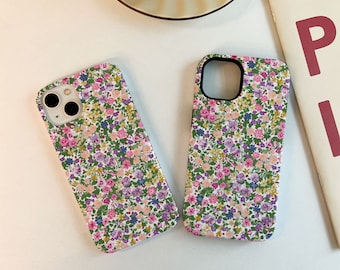 May include: Two phone cases with a floral pattern. The cases are white with small pink, purple, and yellow flowers on a green background.