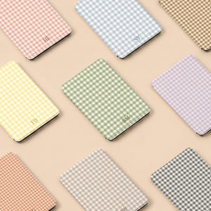 Peut inclure: Une collection d'étuis rectangulaires arborant un motif vichy dans diverses couleurs pastel, notamment rose, bleu, beige, jaune, vert, lavande, orange et gris. Certains étuis sont personnalisés avec des initiales de deux lettres en police serif.