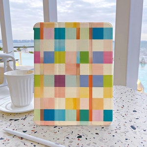 May include: A tablet case featuring a colourful plaid pattern in shades of pink, blue, green, yellow, and orange. The case is made from a soft, textured material and has a sleek, modern design.