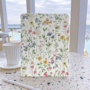May include: A white tablet case with a floral pattern featuring pink, yellow, blue, and green flowers on a white background.