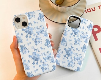 May include: Two white phone cases with a blue floral pattern. The cases are made of a hard plastic material and have a matte finish.