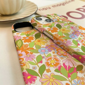 May include: Two phone cases featuring a retro floral design. The pattern includes a range of flowers in shades of orange, pink, yellow, and blue on a cream background. The cases are made from a hard plastic material and have a glossy finish.