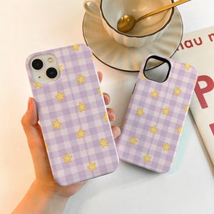 Peut inclure: Deux coques de téléphone avec un motif vichy lavande et blanc et des étoiles jaunes. Les coques sont présentées à côté d'une tasse à thé et d'une soucoupe. Les coques sont conçues pour s'adapter à un smartphone.