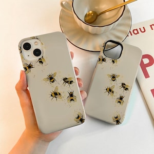 May include: Two beige phone cases with a pattern of yellow and black bees. The cases are made of a hard plastic material and have a matte finish.
