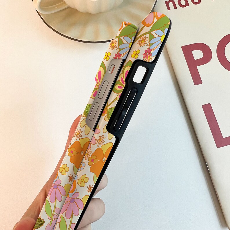 May include: A phone case with a floral design featuring pink, yellow, and orange flowers. The case is black and has a cutout for the camera lens.