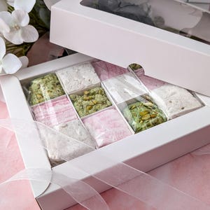 May include: A white box with a clear lid filled with small squares of pink, white, and green marshmallow. The box is tied with a white ribbon.