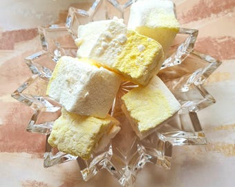 May include: A clear glass dish with a starburst design holds a collection of yellow and white marshmallows. The marshmallows are soft and fluffy, and they are arranged in a random pattern.
