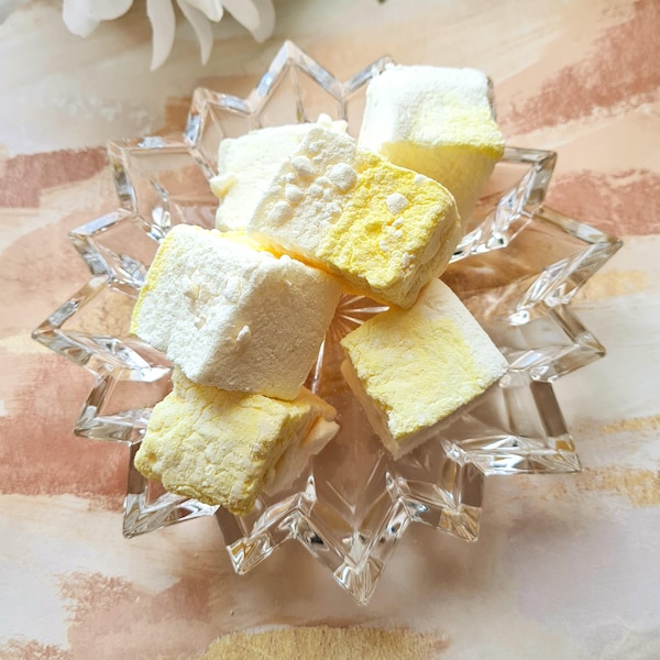 May include: A clear glass dish with a starburst design holds a collection of yellow and white marshmallows. The marshmallows are soft and fluffy, and they are arranged in a random pattern.