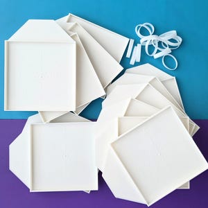 May include: A collection of white origami paper pieces, some folded into geometric shapes, is shown from above. White elastic bands and strips are also present. The background is split between blue and purple.