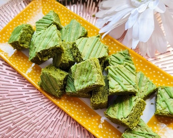 May include: A yellow plate with white polka dots holds a collection of green matcha brownies. The brownies are arranged in a random pattern and have a light green glaze on top.