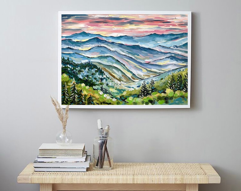 May include: A painting of a mountain landscape with a pink and blue sky. The mountains are painted in shades of blue, green, and yellow. There are trees in the foreground and a valley in the distance.