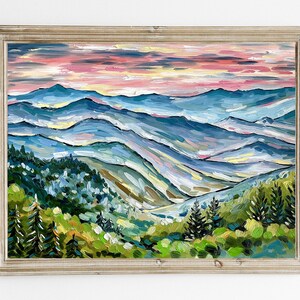 May include: A painting of a mountain landscape with a blue, green, and pink color scheme. The mountains are layered and the sky is a soft pink. The painting is framed in a light wood frame.
