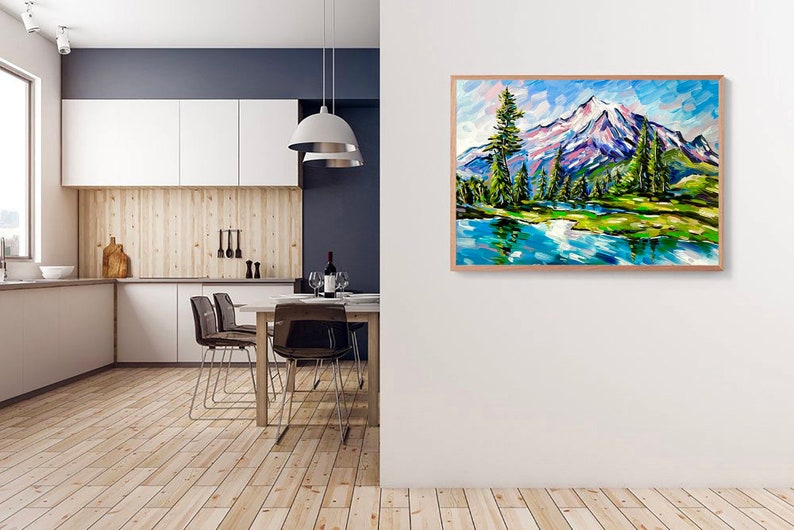 May include: A framed landscape painting depicts a mountain scene with a snow-capped peak, green trees, and a blue lake. The artwork uses bold brushstrokes and vibrant colors, creating a textured effect. The frame is made of light-colored wood.