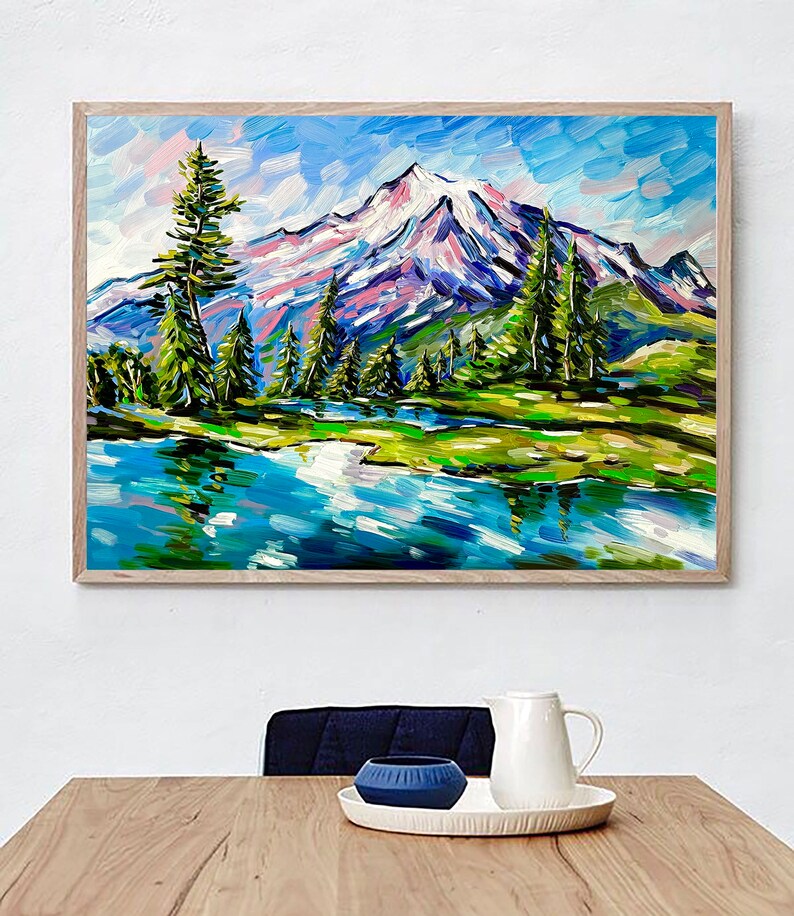 May include: A framed landscape painting depicts a snow-capped mountain range reflected in a blue lake. The artwork features vibrant brushstrokes in shades of blue, green, pink, and white, with tall green trees lining the water's edge. The painting is in a light brown wooden frame.