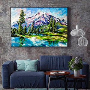 May include: A framed landscape painting depicts a mountain range with snow-capped peaks, lush green trees, and a serene blue lake. The artwork uses bold brushstrokes and vibrant colors, including blues, greens, and purples, to create a textured effect.