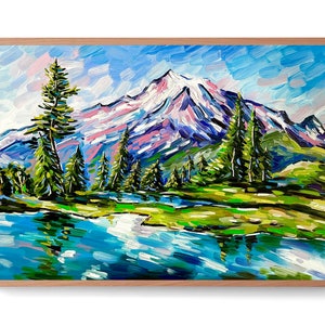 May include: A framed landscape painting depicts a snow-capped mountain range under a blue sky. The artwork features a lake in the foreground, with green trees and grass. The painting uses thick brushstrokes and vibrant colors.