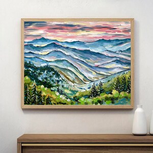May include: A painting of a mountain landscape with a pink and blue sky. The mountains are painted in shades of blue, green, and yellow. The painting is framed in a light wood frame.