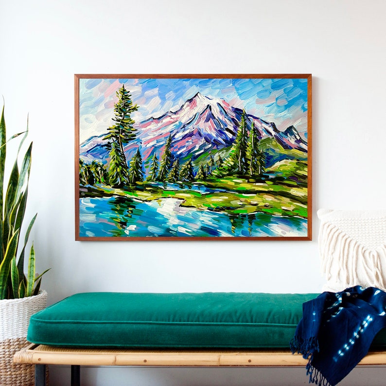 May include: A framed landscape painting depicts a mountain scene with a snow-capped peak, a reflective lake, and evergreen trees. The artwork uses thick brushstrokes in shades of blue, green, pink, and white, creating a textured effect. The frame is a warm brown color.