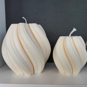 May include: Two white, swirl-shaped candles with a textured surface. The larger candle is in the background and the smaller candle is in the foreground.