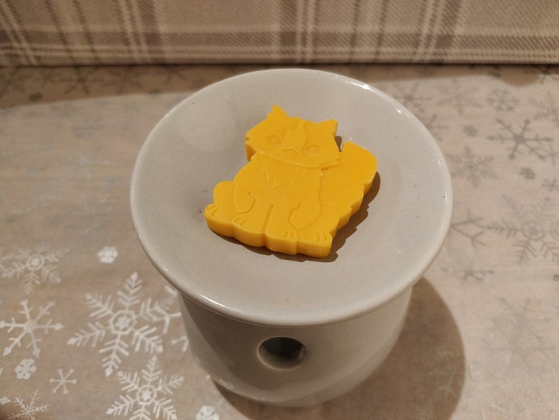 May include: A yellow wax melt shaped like a cat sitting on a white ceramic wax warmer.