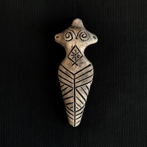 May include: A small, ceramic figurine of a woman with geometric patterns and a stylized face. The figurine is painted in shades of brown and black.