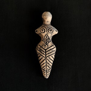 May include: A small, brown clay figurine of a woman with geometric designs. The figurine is standing upright with its arms outstretched.