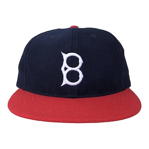 May include: A navy blue baseball cap with a red brim and a white embroidered "B" logo. The cap has a classic, flat-brim design and a red button on top. This hat is a stylish accessory for sports fans.