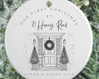 May include: White ceramic Christmas bauble featuring a black and white illustration of a house with a wreath on the door. The text on the bauble reads "Our First Christmas at 21 Honey Road Simon & Sarah 2024".