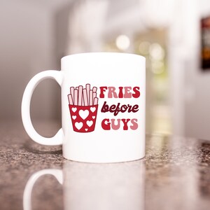 May include: White ceramic mug with a red and pink graphic of french fries in a red container with pink hearts and the text "FRIES before GUYS".