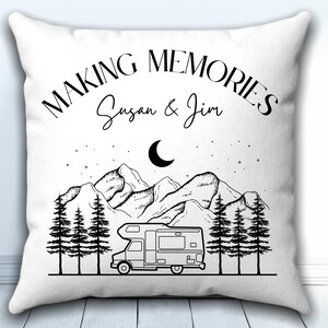 May include: A white square throw pillow featuring a black line art illustration of a camper van parked in front of pine trees and mountains under a crescent moon and stars. The text reads "MAKING MEMORIES" and "Susan & Jim".