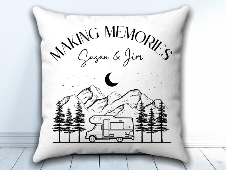 May include: A white square throw pillow featuring a black line art illustration of a camper van parked in front of pine trees and mountains under a crescent moon and stars. The text reads "MAKING MEMORIES" and "Susan & Jim".