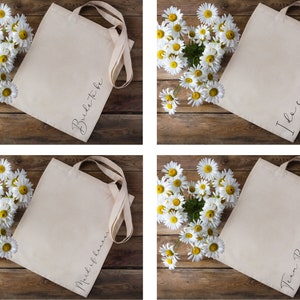 May include: Four canvas tote bags with long handles, each with a different script text: "Bride to be", "I do crew", "Maid of honor", and "Team Bride". The bags are beige and are arranged on a wooden surface with a heart-shaped arrangement of white daisies.