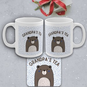 May include: Two white ceramic mugs with a blue and white pattern and a brown bear illustration. The mugs say "Grandpa's Tea" on them. A matching coaster with the same design is also shown.