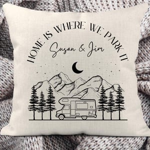 May include: A square off-white throw pillow featuring a black line art graphic of a camper van, pine trees, mountains, a crescent moon, and stars. The text reads "HOME IS WHERE WE PARK IT" above the names "Susan & Jim" in black ink.
