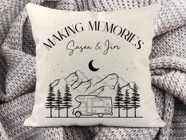 May include: A square off-white throw pillow featuring a black line art illustration of a camper van, pine trees, mountains, a crescent moon, and stars. The text reads "MAKING MEMORIES" and "Susan & Jim" in a black serif and script font.