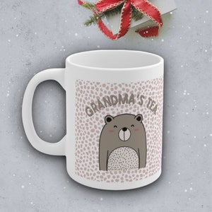May include: White ceramic mug with a pink and white polka dot pattern. The mug has a brown bear illustration and the text "Grandma's Tea" in black.