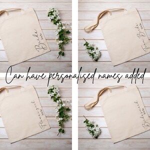 May include: Four beige tote bags with different text: "Bride", "Team Bride", "Flower Girl", and "Bridesmaid". Each bag has a cream-colored handle and is decorated with white flowers. The text "Can have personalised names added" is also present.