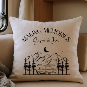 May include: A square off-white throw pillow featuring a black line art graphic of a camper van, pine trees, mountains, and a crescent moon. The text "MAKING MEMORIES" is printed in a curved font above the names "Susan & Jim" in script.