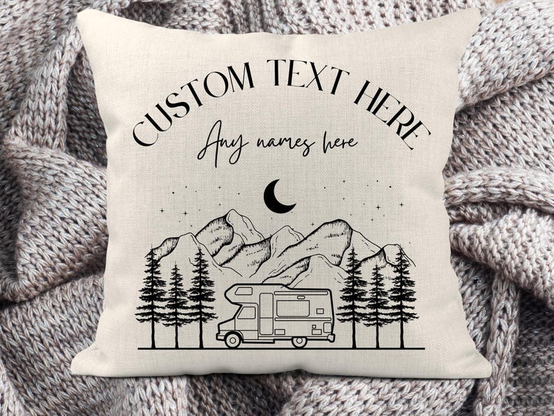 May include: A square off-white throw pillow featuring a black line art illustration of a camper van, pine trees, mountains, and a crescent moon. The text CUSTOM TEXT HERE and Any names here is printed in black ink on the upper portion.