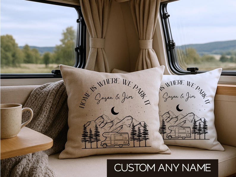 May include: Two square throw pillows with a beige fabric cover featuring a black line art graphic of a camper van, pine trees, mountains, and a crescent moon. The text reads "HOME IS WHERE WE PARK IT" and "Susan & Jim".